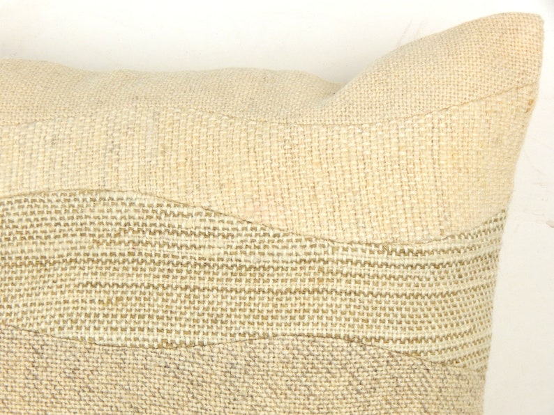 Op de afbeelding: Close-up van een beige decoratief kussen met een textuur, geweven ontwerp. Het kussen heeft horizontale banden van verschillende texturen en tinten beige, waardoor een gelaagd effect ontstaat. Het is een neutraal woondecoratie-item.