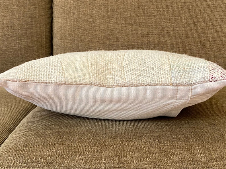 May include: A rectangular pillow with a patchwork design. The top section features a textured, off-white fabric with rectangular patches. The bottom section is a solid, light pink fabric. The pillow is resting on a brown surface.