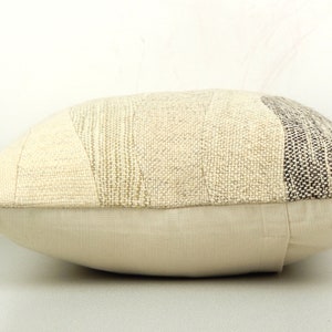 Op de afbeelding: Een rechthoekig sierkussen met een patchwork-ontwerp. Het bovenste gedeelte heeft verschillende stoffen met textuur in cr&egrave;me-, beige- en grijstinten. Het onderste gedeelte is een effen, lichtbeige stof. Het kussen is voor de woondecoratie.