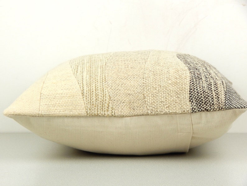 Op de afbeelding: Een rechthoekig sierkussen met een patchwork-ontwerp. Het bovenste gedeelte heeft verschillende stoffen met textuur in cr&egrave;me-, beige- en grijstinten. Het onderste gedeelte is een effen, lichtbeige stof. Het kussen is voor de woondecoratie.