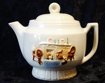 May include: White ceramic teapot with a brown and white scene of a fireplace and a cat on the side. The teapot has a lid and a handle.