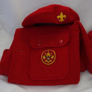 May include: Red wool Boy Scout uniform with a red beret, a pocket with a BSA emblem, and a gold embroidered scout emblem on the beret.