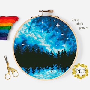 Puede incluir: Patrón de punto de cruz de un cielo nocturno estrellado con una silueta de bosque en primer plano. El cielo es un degradado de azul y blanco con estrellas blancas. El bosque es negro. El patrón está en un aro de bordado redondo.