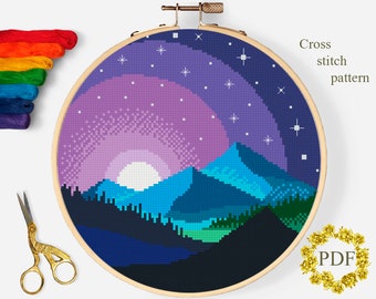 May include: Cross stitch pattern of a purple and blue mountain landscape with a full moon and stars in the sky. The pattern is displayed in a wooden embroidery hoop.