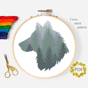 May include: A cross stitch pattern featuring a wolf silhouette made up of green and gray trees. The pattern is displayed in a wooden embroidery hoop. The text "Cross stitch pattern" is visible in the upper right corner of the image. The text "PDF" is visible in a gold wreath in the lower right corner of the image.