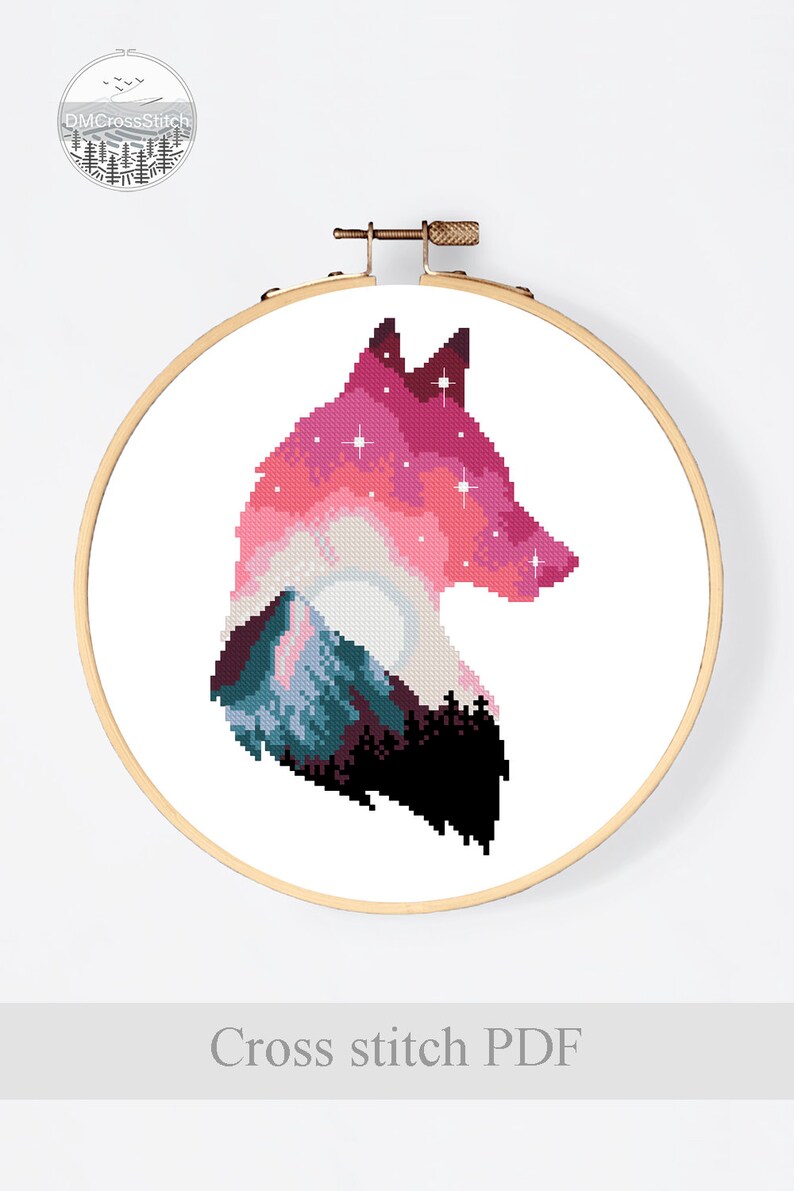 Puede incluir: Patr&oacute;n de punto de cruz de una silueta de lobo con una monta&ntilde;a y un cielo estrellado en su interior. El lobo es rosa, morado y azul, con un contorno negro. El patr&oacute;n est&aacute; en un aro de bordado de madera.
