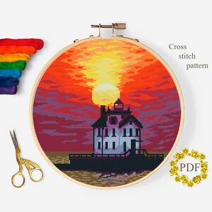Pode incluir: Um padrão de ponto cruz de um pôr do sol sobre uma casa, exibido em um bastidor de bordado de madeira. O pôr do sol apresenta tons de laranja, vermelho e amarelo. A casa é branca com detalhes em rosa. O texto "Cross stitch pattern" e "PDF" são visíveis.
