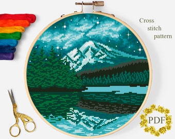 May include: A cross stitch pattern featuring a mountain range with a lake in the foreground. The sky is a dark blue with white clouds and stars. The mountains are a light blue and white, and the lake is a dark blue. The pattern is in a round wooden embroidery hoop.