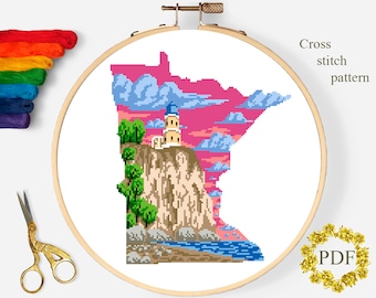 May include: Cross stitch pattern of the state of Minnesota with a lighthouse on a cliff overlooking a body of water. The sky is pink and orange with clouds. The pattern is in a hoop.