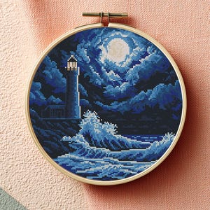 Könnte beinhalten: Eine Kreuzstich-Stickerei mit einer Leuchtturmszene. Das Design zeigt einen hohen, weißen Leuchtturm mit hellem Licht, vor einem dunkelblauen Nachthimmel mit Vollmond und tosenden Wellen. Die Stickerei ist in einem runden Holzrahmen gefasst.
