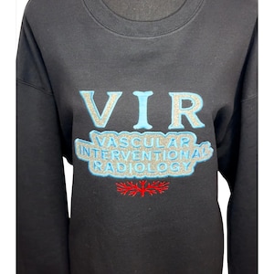 May include: Black crewneck sweatshirt with the text "VIR VASCULAR INTERVENTIONAL RADIOLOGY" in light blue and silver lettering. A red floral design is below the text. The sweatshirt is displayed on a black mannequin.