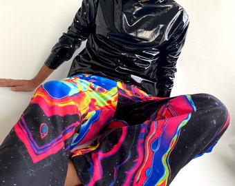 May include: A black, glossy, hooded jacket and vibrant, patterned pants. The pants feature a colorful, abstract design with shades of blue, red, and yellow against a black background. The jacket has long sleeves and a high collar.