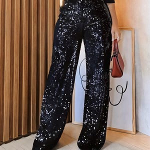 May include: Black wide-leg trousers with a sparkly, sequin fabric. The trousers have a high waist and a relaxed fit.