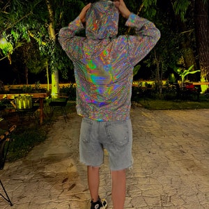 K&ouml;nnte beinhalten: Eine Person tr&auml;gt einen silbernen, regenbogenfarbenen Hoodie mit einer Kapuze mit Kordelzug und langen &Auml;rmeln. Die Person tr&auml;gt eine blaue Jeans-Shorts und schwarz-wei&szlig;e Turnschuhe.