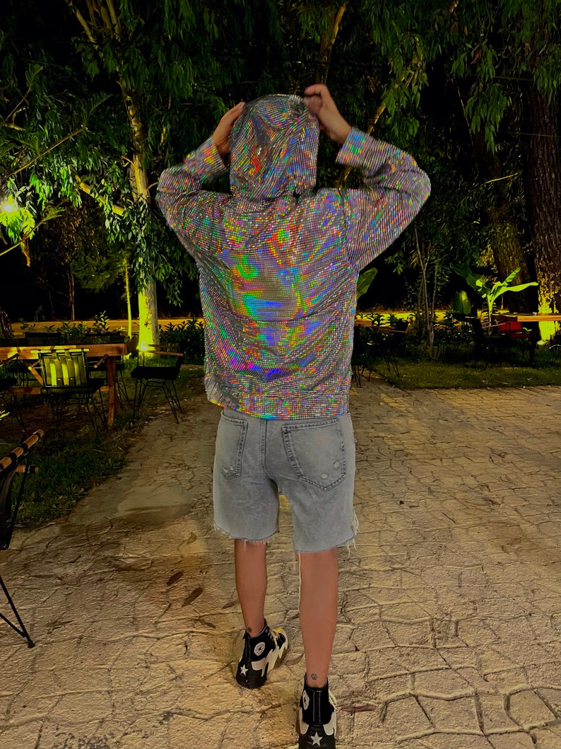 K&ouml;nnte beinhalten: Eine Person tr&auml;gt einen silbernen, regenbogenfarbenen Hoodie mit einer Kapuze mit Kordelzug und langen &Auml;rmeln. Die Person tr&auml;gt eine blaue Jeans-Shorts und schwarz-wei&szlig;e Turnschuhe.