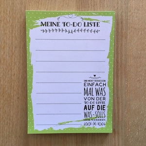 Könnte beinhalten: Ein grüner Notizblock für To-Do-Listen mit weißen Linien und dem Text "MEINE TO-DO LISTE" oben. Am unteren Rand des Notizblocks steht der Text "UND NICHT VERGESSEN: EINFACH MAL WAS VON DER TO-DO LISTE AUF DIE WAS-SOLLS LISTE SCHREIBEN".