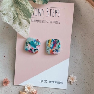 Peut inclure: Une paire de boucles d'oreilles carrées avec un motif floral sur fond bleu clair. Les boucles d'oreilles sont faites à la main à Londres par Tiny Steps.