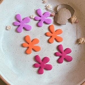 Könnte beinhalten: Sechs bunte Filzblumenformen in einer weißen Keramikschale. Die Blumen sind in den Farben Rosa, Lila und Orange.