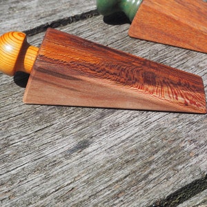 Könnte beinhalten: Ein Holz-Türstopper mit einem abgerundeten Knopf an der Oberseite. Der Türstopper ist aus dunklem Holz mit einem rötlichen Farbton und einem natürlichen Holzmaserungsmuster.
