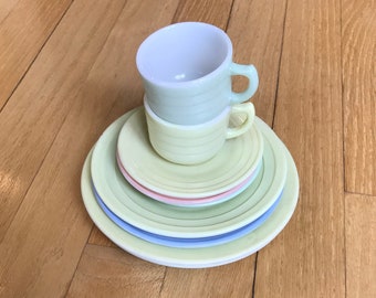 May include: A set of pastel-colored children's teacups and saucers. The cups and saucers are stacked on top of each other. The cups are white with a light green rim and the saucers are light green, light blue, and pink.