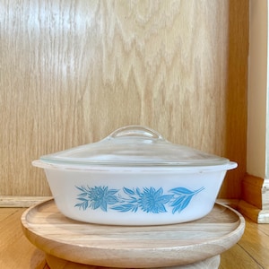 May include: A white oval baking dish with a blue floral design. The dish is on a wooden stand.