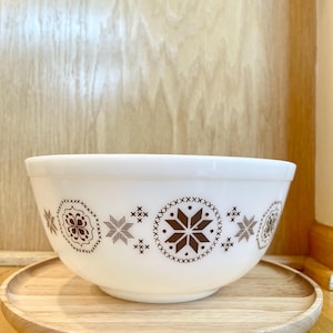 May include: White mixing bowl with a brown snowflake pattern. The bowl is sitting on a wooden stand.