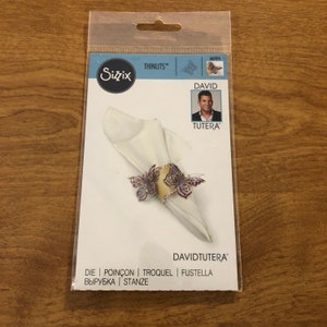 May include: A Sizzix Thinlits die set with a butterfly design, wrapped around a white napkin. The packaging features the name "DAVID TUTERA" and the words "DIE | POINÇON | TROQUEL | FUSTELLA | ВЫРУБКА | STANZE".