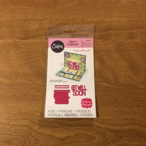 May include: A packet of Sizzix Thinlits 3-D Drop-Ins die cuts for crafting. The package shows a sample card with the words "Get Well Soon" and floral accents. The package also includes the words "Stephanie Barnard".
