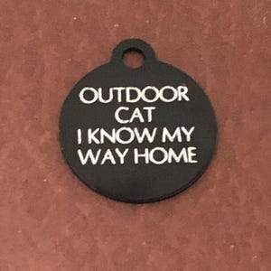 May include: Black round cat tag with white text that reads "Outdoor Cat I Know My Way Home".