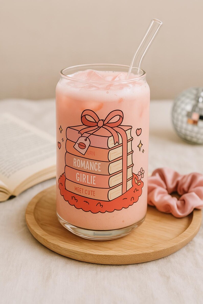 May include: A pink glass can with a straw, filled with a pink beverage. The can has a graphic of a stack of books tied with a pink ribbon, with the words "Born", "Romance", "Girlie", and "Meet Cute" on the books.
