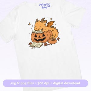 Peut inclure: T-shirt blanc avec un dessin anim&eacute; d'un dragon sur une citrouille d'Halloween lisant un livre. Le dragon est orange avec des ailes et des cornes. La citrouille est orange avec un visage sculpt&eacute;. Le t-shirt comprend le texte "svg & png files &bull; 300 dpi &bull; digital download".