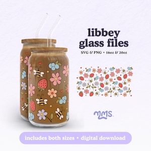 Puede incluir: Dos vasos de vidrio con tapas de madera y pajitas transparentes. Los vasos están decorados con flores coloridas, fresas y abejas. El texto "libbey glass files" se muestra encima de un patrón floral.