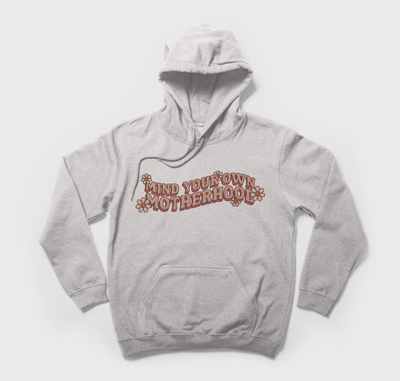May include: A gray hooded sweatshirt with the text "MIND YOUR OWN MOTHERHOOD" in pink and brown letters with pink flowers on either side of the text.