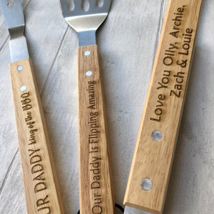 May include: Set of three wooden handled grilling tools with engraved messages. The spatula has the message "Our Daddy Is Flipping Amazing". The fork has the message "Our Daddy King of the BBQ". The tongs have the message "Love You Olly, Archie, Zach & Louie".