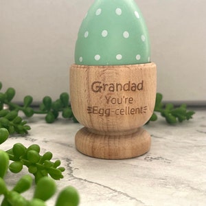 May include: A wooden egg cup with a green and white polka dot egg inside. The egg cup is engraved with the text "Grandad You're Egg-cellent".