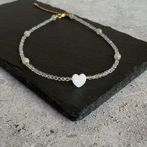 Pode incluir: Um colar delicado com um pingente de coração branco, contas transparentes e uma corrente dourada.