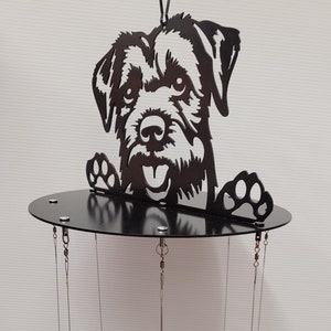 May include: Black metal wind chime featuring a silhouette of a terrier dog peeking over the top. The chime has eight smaller dog silhouettes hanging from the bottom.