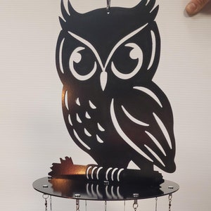 May include: Black metal owl wind chime with multiple smaller owls hanging from the base. The large owl is perched on a round base with a hook at the top.