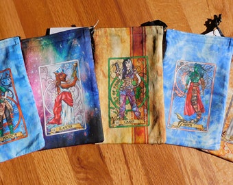 May include: Five colorful fabric dice bags with different tarot card designs. The bags are blue, black, brown, blue, and brown. The tarot cards feature illustrations of people and mythical creatures.
