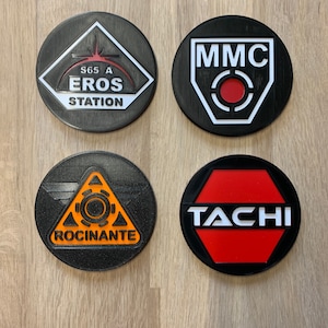 May include: Four round black coasters with white and red designs. The coasters feature the text "S65 A EROS STATION", "MMC", "ROCINANTE", and "TACHI".