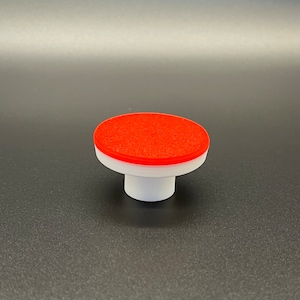 May include: A red and white plastic button with a textured top. The button is round and has a short, white stem.
