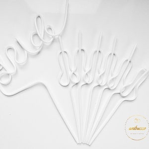 May include: White plastic straws bent into the word "bride" on a white background. The straws are arranged in a fan shape with the word "bride" at the top. The straws are all the same size and shape. The background is a plain white surface.