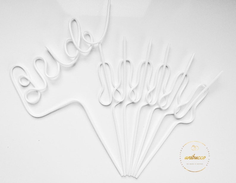May include: White plastic straws bent into the word "bride" on a white background. The straws are arranged in a fan shape with the word "bride" at the top. The straws are all the same size and shape. The background is a plain white surface.