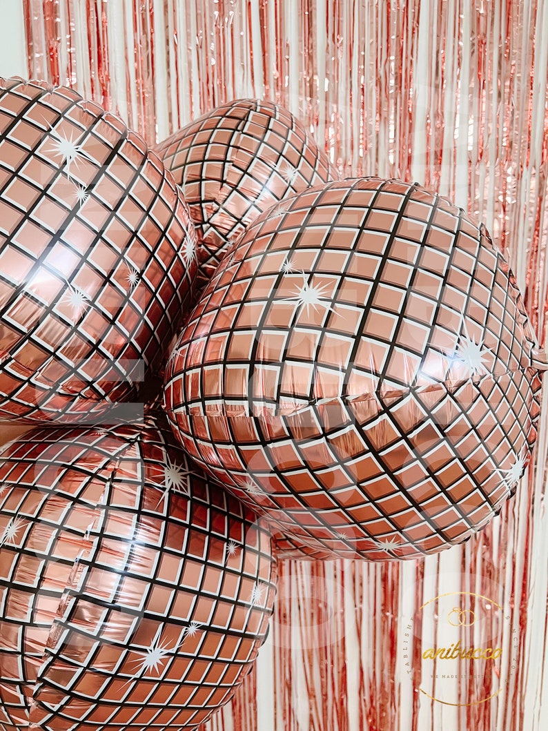 May include: A cluster of four round, rose gold foil balloons featuring a printed grid pattern that mimics the reflective surface of a disco ball. Each balloon has white starburst accents on the grid, creating a shiny, metallic appearance.