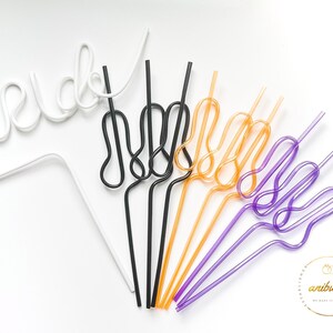 May include: A set of colorful, bendable drinking straws in white, black, orange, purple, and pink. The straws are shaped into a fun, whimsical design.