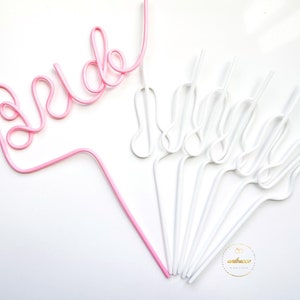 May include: Pink and white plastic straws shaped to spell "bride" and "maid of honor".