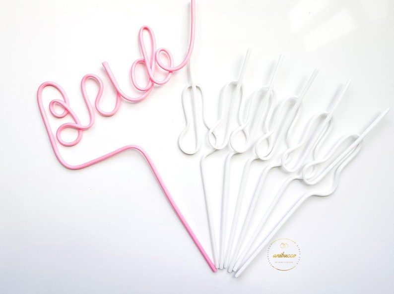 May include: Pink and white plastic straws shaped to spell "bride" and "maid of honor".
