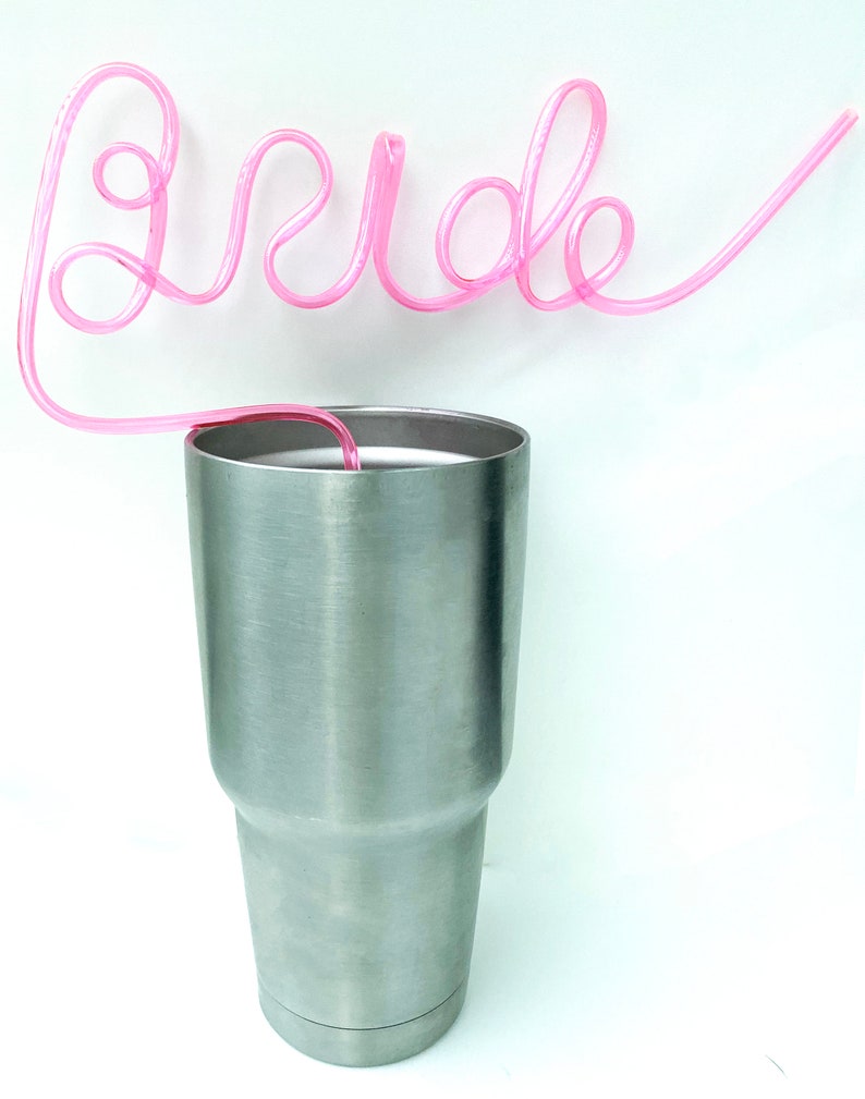 May include: A silver stainless steel tumbler with a pink plastic straw shaped to spell out the word "bride".