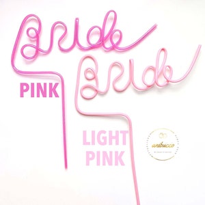 May include: Two pink plastic straws shaped to spell out the word "bride". The top straw is a darker pink and the bottom straw is a lighter pink. The straws are on a white background.