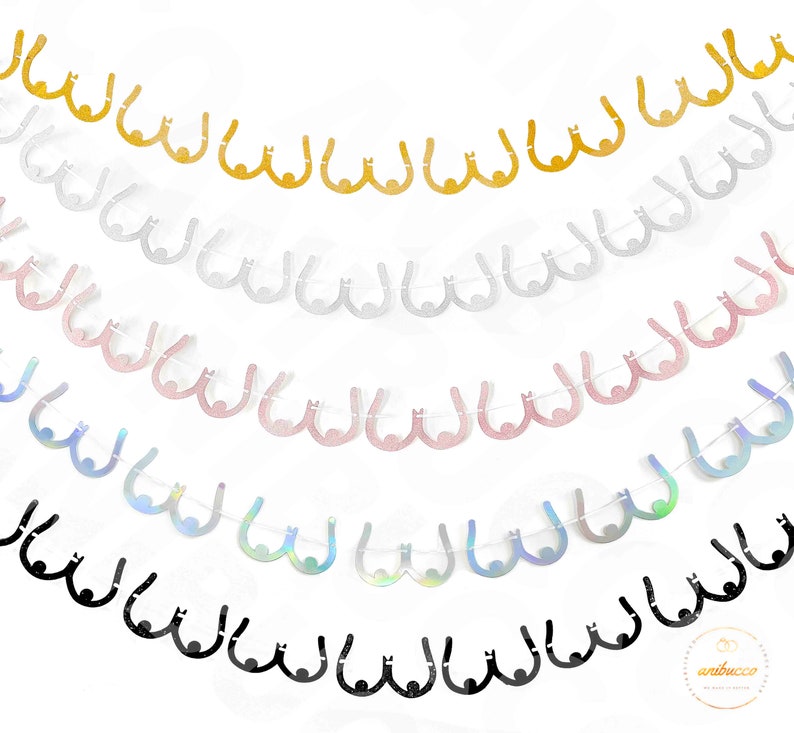May include: A garland of six rows of glitter paper cutouts in the shape of breasts. The garland is made of gold, silver, pink, iridescent, and black glitter paper.